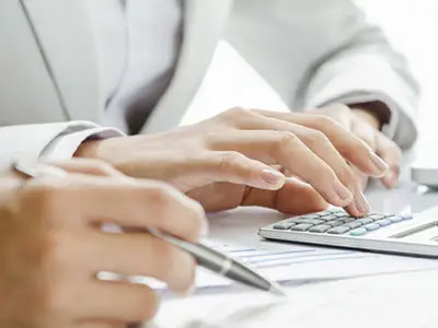 Close-up of hands typing on a calculator and writing notes, symbolizing financial planning and accounting work in a professional setting.