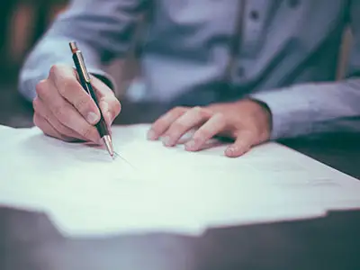 Person writing on a sheet of paper with a pen, showcasing a focus on documentation or note-taking in a professional setting.
